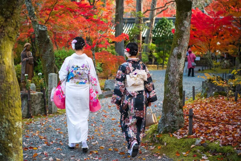 Mujeres japonesas con kimono tradicional caminando por el jardín del templo Shinnyodo durante el otoño con vibrantes hojas de arce rojas, mostrando una fotografía perfecta de kimono con follaje otoñal en Kioto.