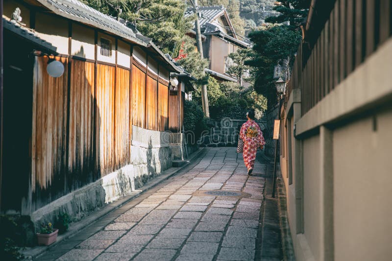 Tranquilo callejón tradicional en el distrito Gion de Kioto con una mujer japonesa con kimono caminando por calles históricas, capturando el auténtico estilo de vida japonés antiguo y la arquitectura tradicional.
