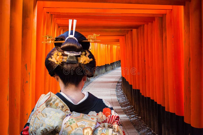Mujer con kimono tradicional caminando por el famoso túnel de las mil puertas torii en el santuario Fushimi Inari Taisha en Kioto, mostrando una composición fotográfica perfecta con kimono.