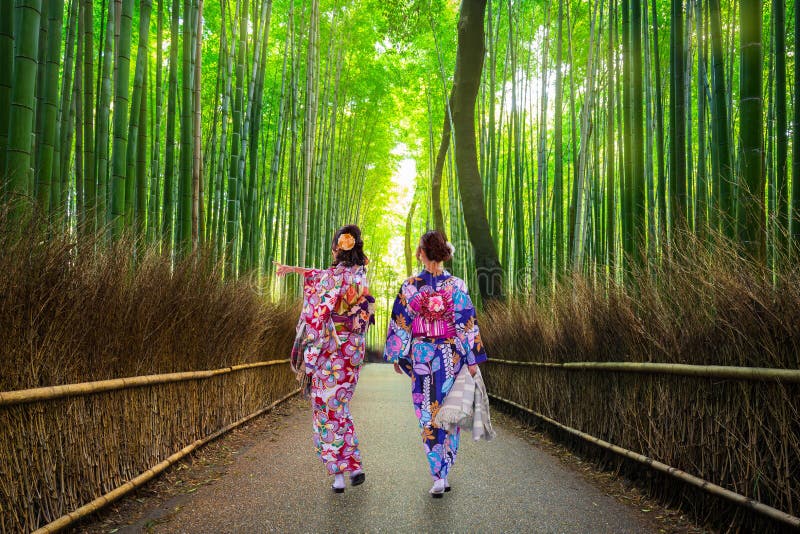 Dos mujeres vestidas con coloridos kimonos tradicionales caminan por el famoso bosque de bambú de Arashiyama en Kioto, demostrando la fotografía ideal con kimono en un entorno de bosque natural japonés.